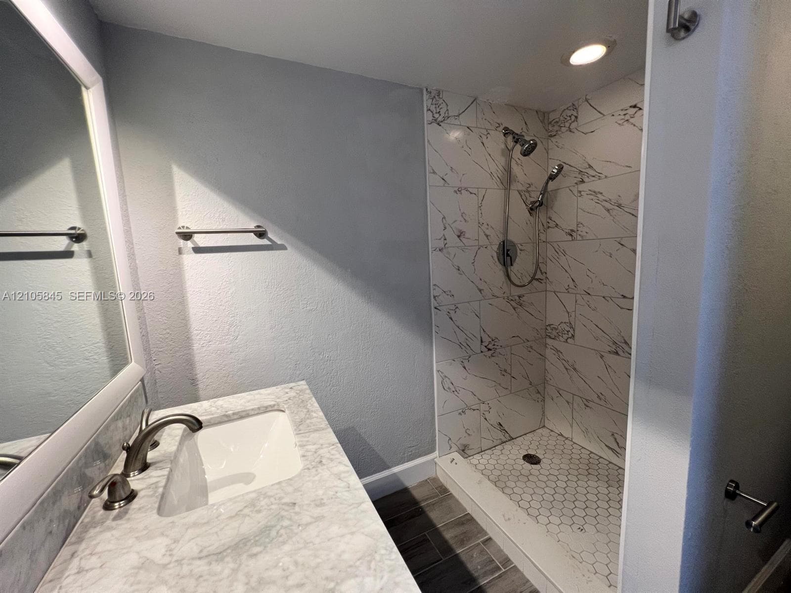 Bathroom featuring a vanity with a stone-top counter, undermount sink, and metallic faucet, paired with a walk-in shower showcasing large-format wall tile, hexagonal floor tile, and a multi-head shower system