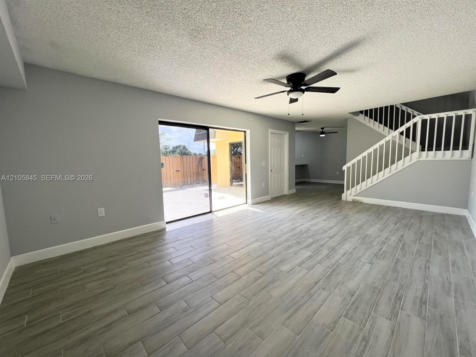 Open-concept interior featuring wood-finish tile flooring, a sliding glass door, white stair railing, and a ceiling fan