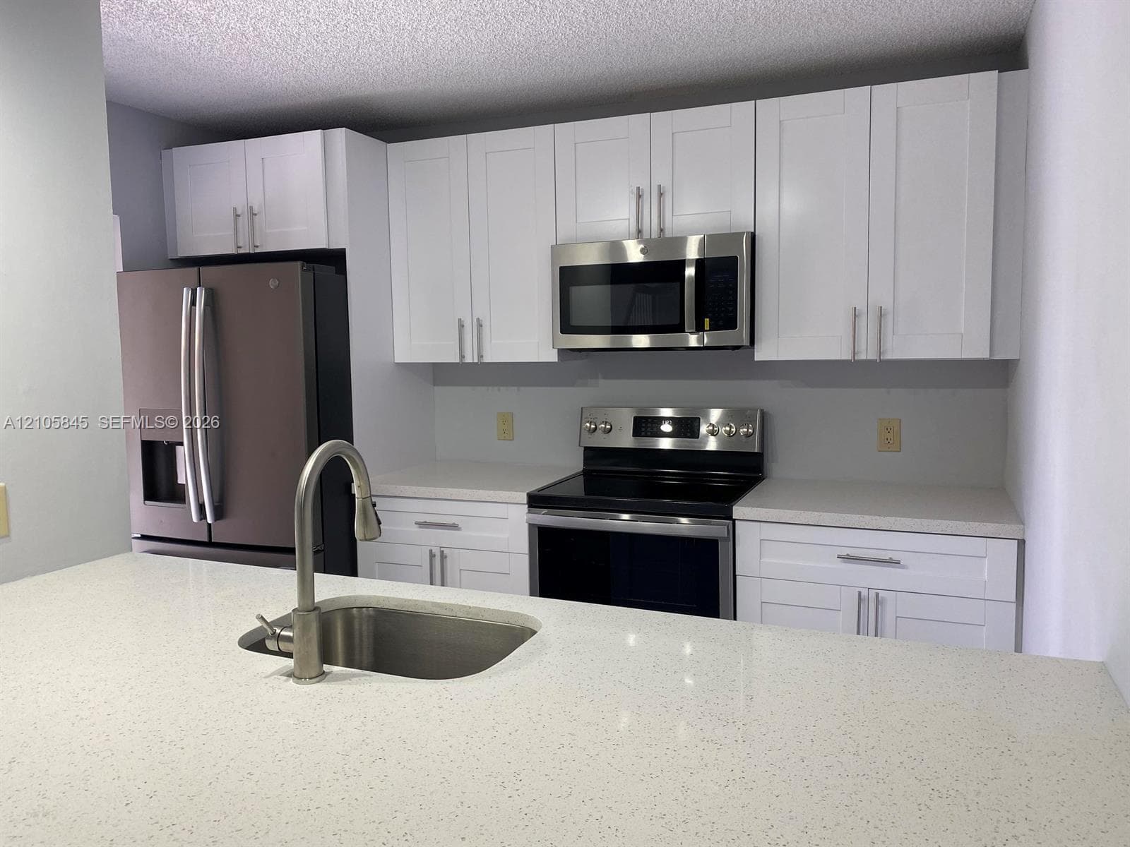 Kitchen featuring white shaker-style cabinetry, solid-surface countertops, stainless steel appliances, and an undermount sink with a high-arch pull-down faucet