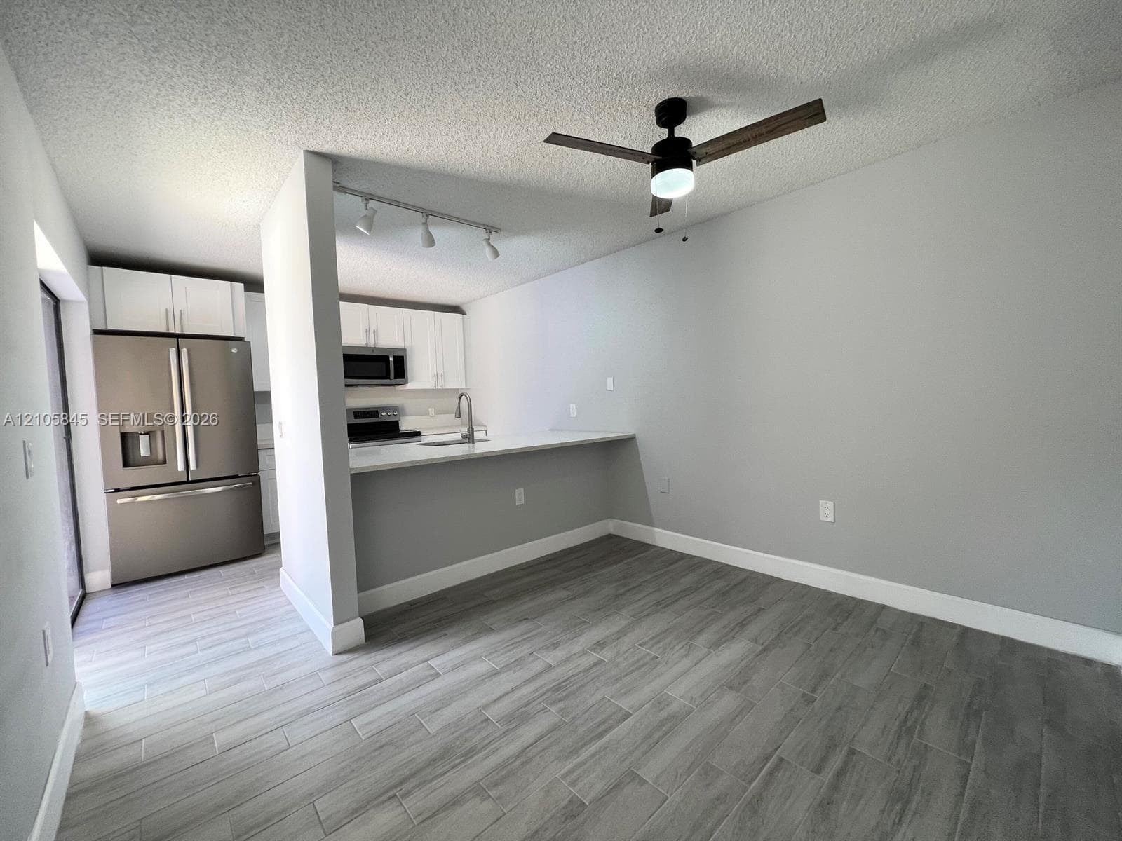 Kitchen featuring stainless steel appliances, white cabinetry, a peninsula with stone-finish countertops, wood-finish flooring, and a ceiling fan with integrated lighting