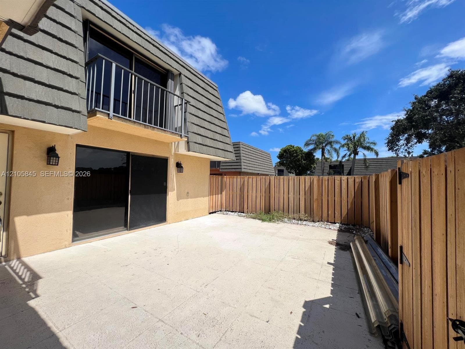 Exterior patio featuring concrete paving, privacy wood fencing, and a second-story balcony with metal railing