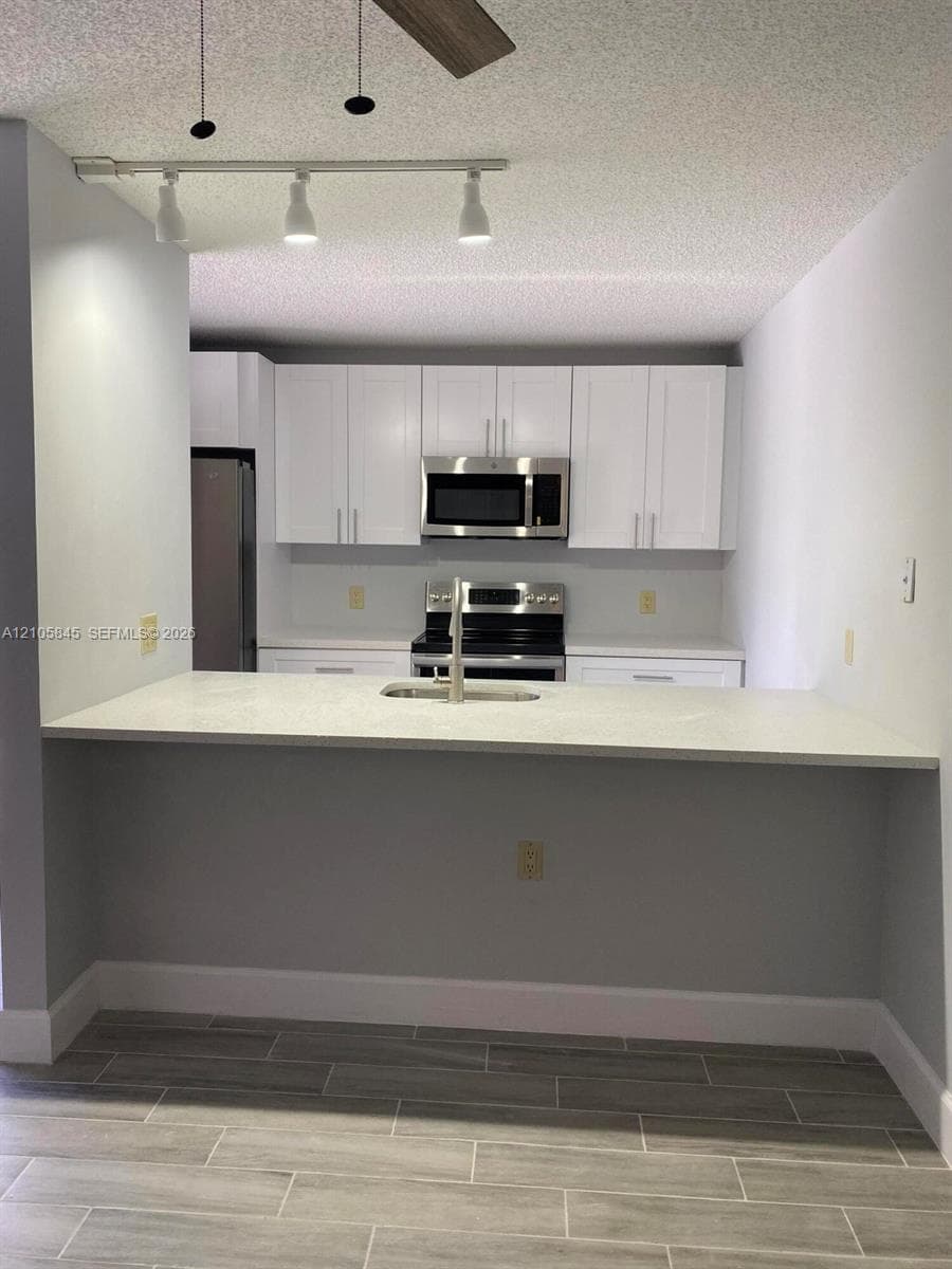 Kitchen featuring white cabinetry, solid-surface countertops, wood-finish tile flooring, a stainless steel over-the-range microwave, and a peninsula-style sink