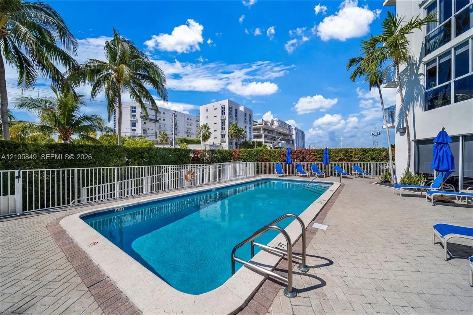 Aerial perspective of a high-rise residential building featuring an outdoor swimming pool, landscaped grounds, and proximity to the coastline