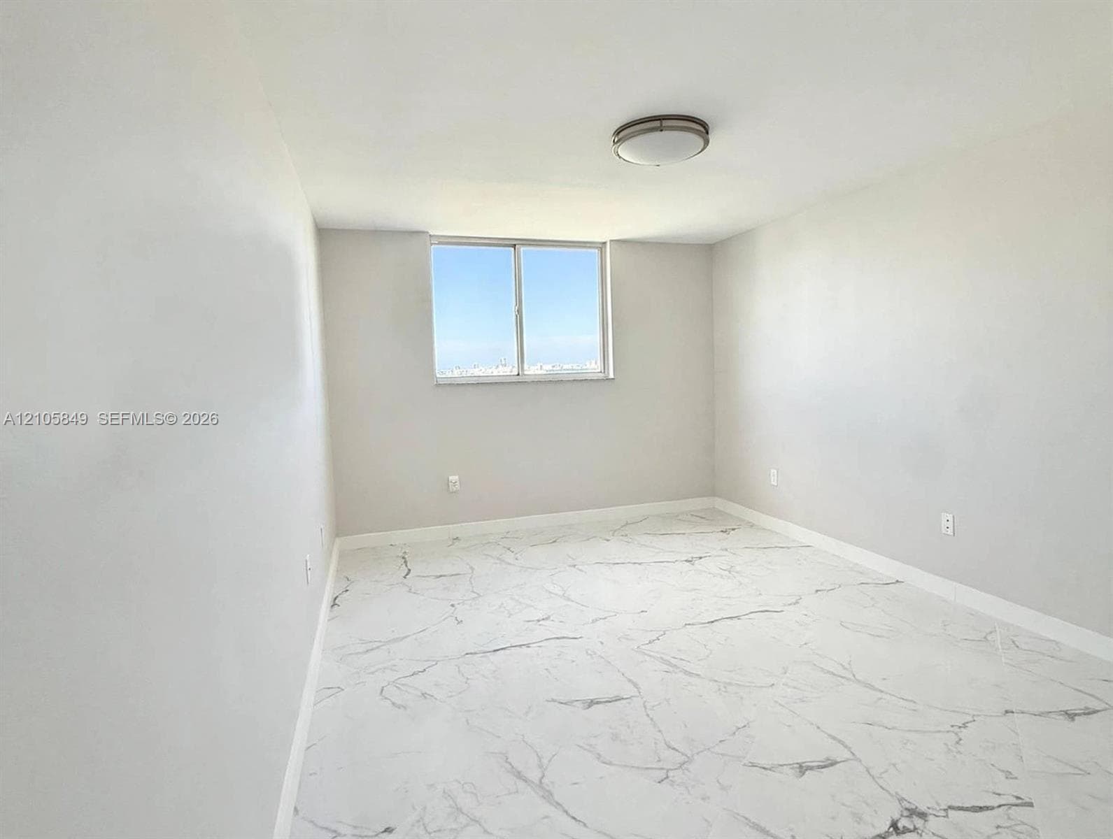 Large-format tile flooring with veined detailing, neutral wall tones, flush-mount ceiling light fixture, and a single sliding window