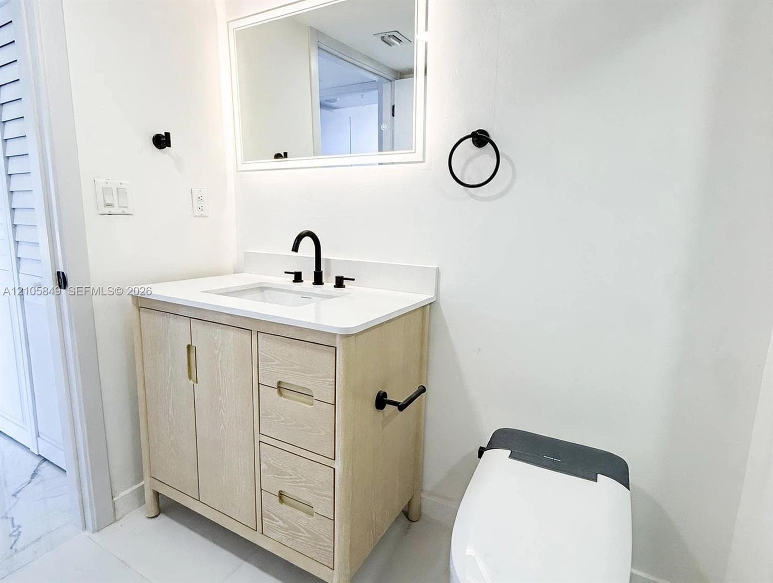 Light wood-finish vanity with a white countertop, undermount sink, matte black faucet, and walk-in shower featuring patterned tile surrounds and a matte black rainfall showerhead