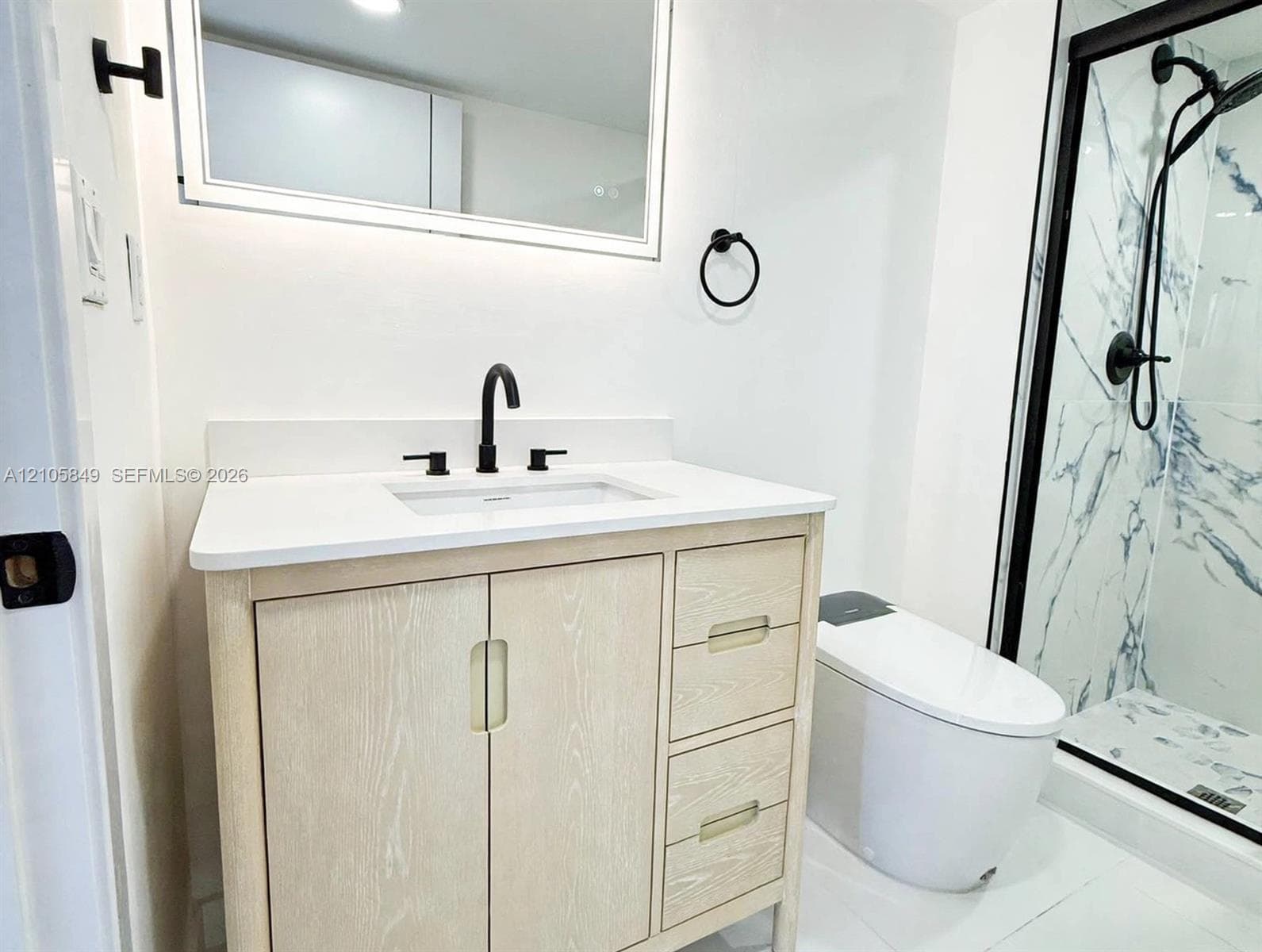 Light-finish wood vanity with a white countertop, rectangular undermount sink, integrated LED-lit mirror, and matte black fixtures