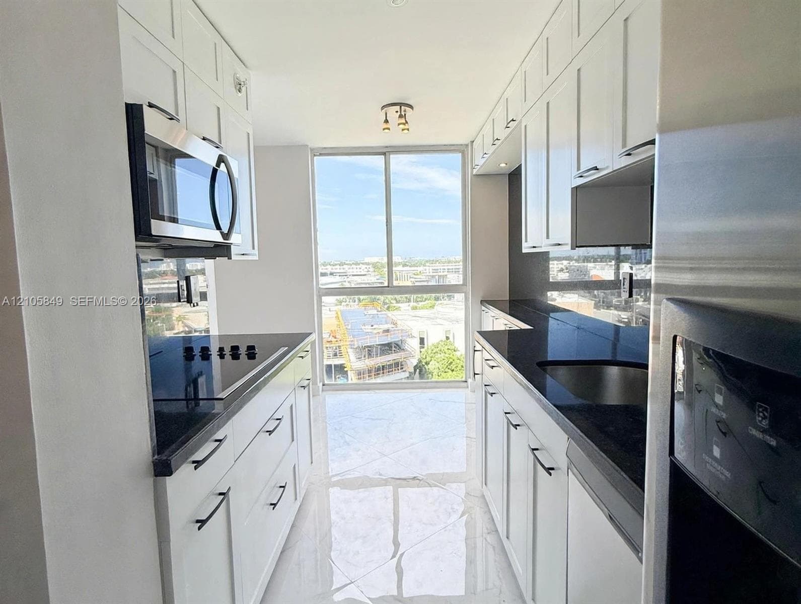 Large-format tiled flooring with veined detailing, white cabinetry, stainless steel appliances, and sliding glass door access to an exterior balcony