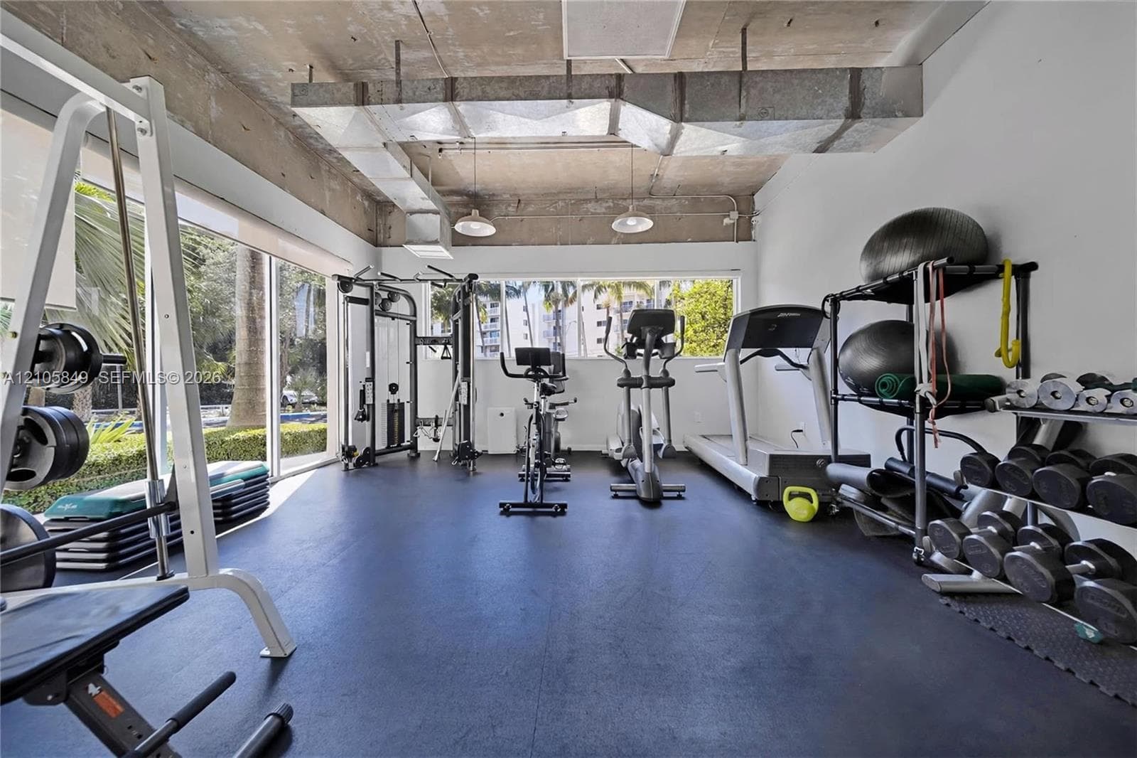 Fitness area featuring exposed concrete ceilings, expansive floor-to-ceiling windows, rubberized flooring, and industrial-style pendant lighting