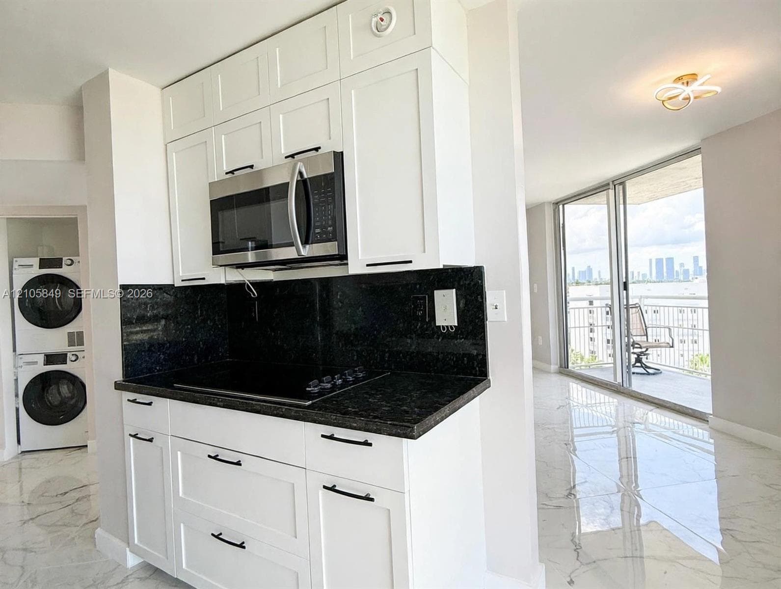 White Shaker cabinetry with matte black hardware, dark stone countertops, full-height stone backsplash, stainless steel undermount sink with a gooseneck faucet, and polished large-format tile flooring