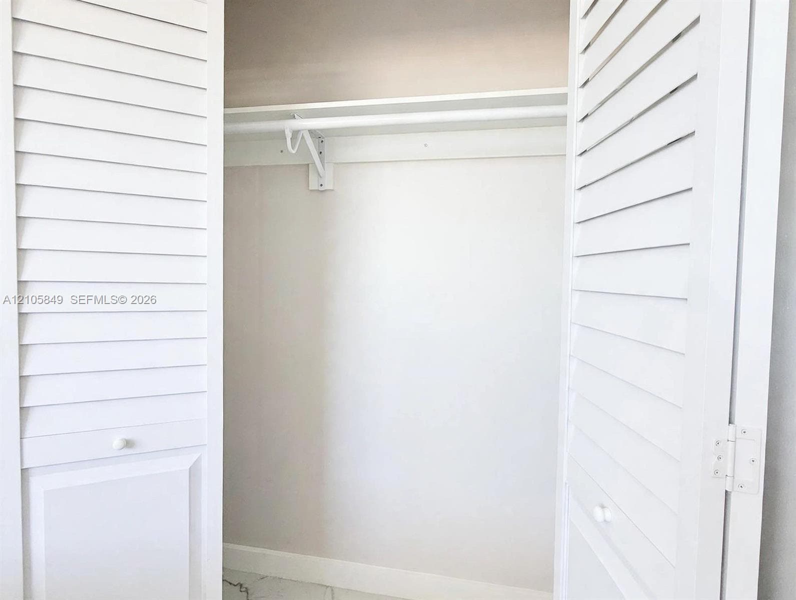 Stacked white laundry appliance set enclosed within a built-in alcove featuring white louvered bifold doors