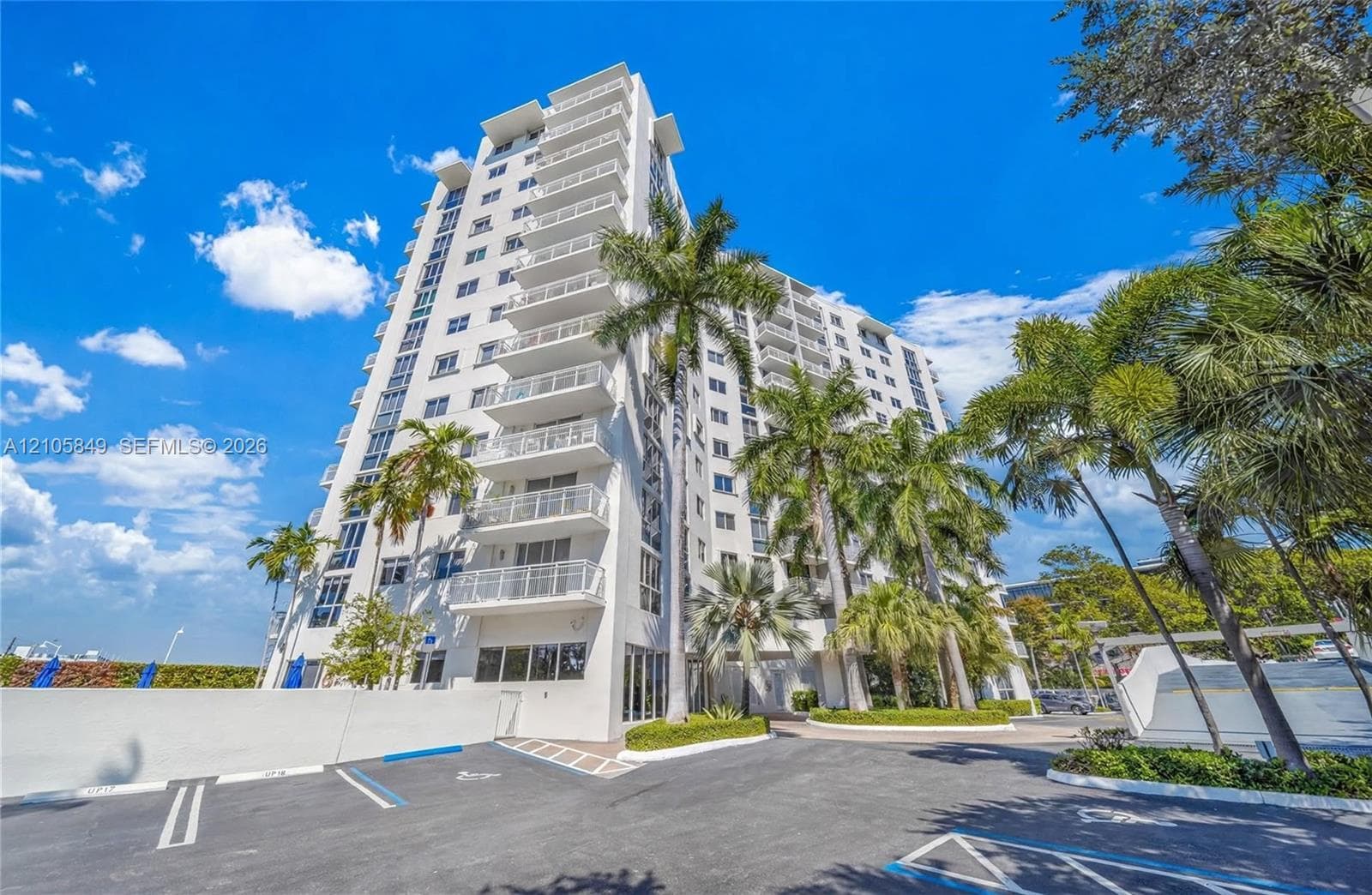 Aerial perspective of mid-rise residential building featuring a rooftop pool, private surface parking, and proximity to the waterfront
