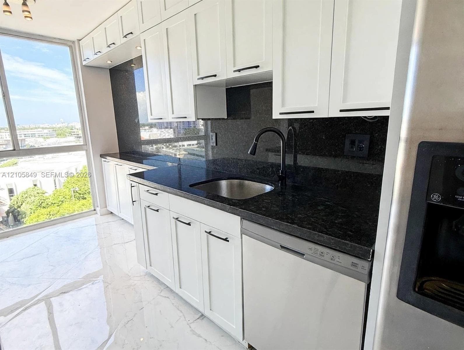Galley kitchen featuring white Shaker-style cabinetry, dark stone countertops, stainless steel appliances, large-format tile flooring, and floor-to-ceiling windows