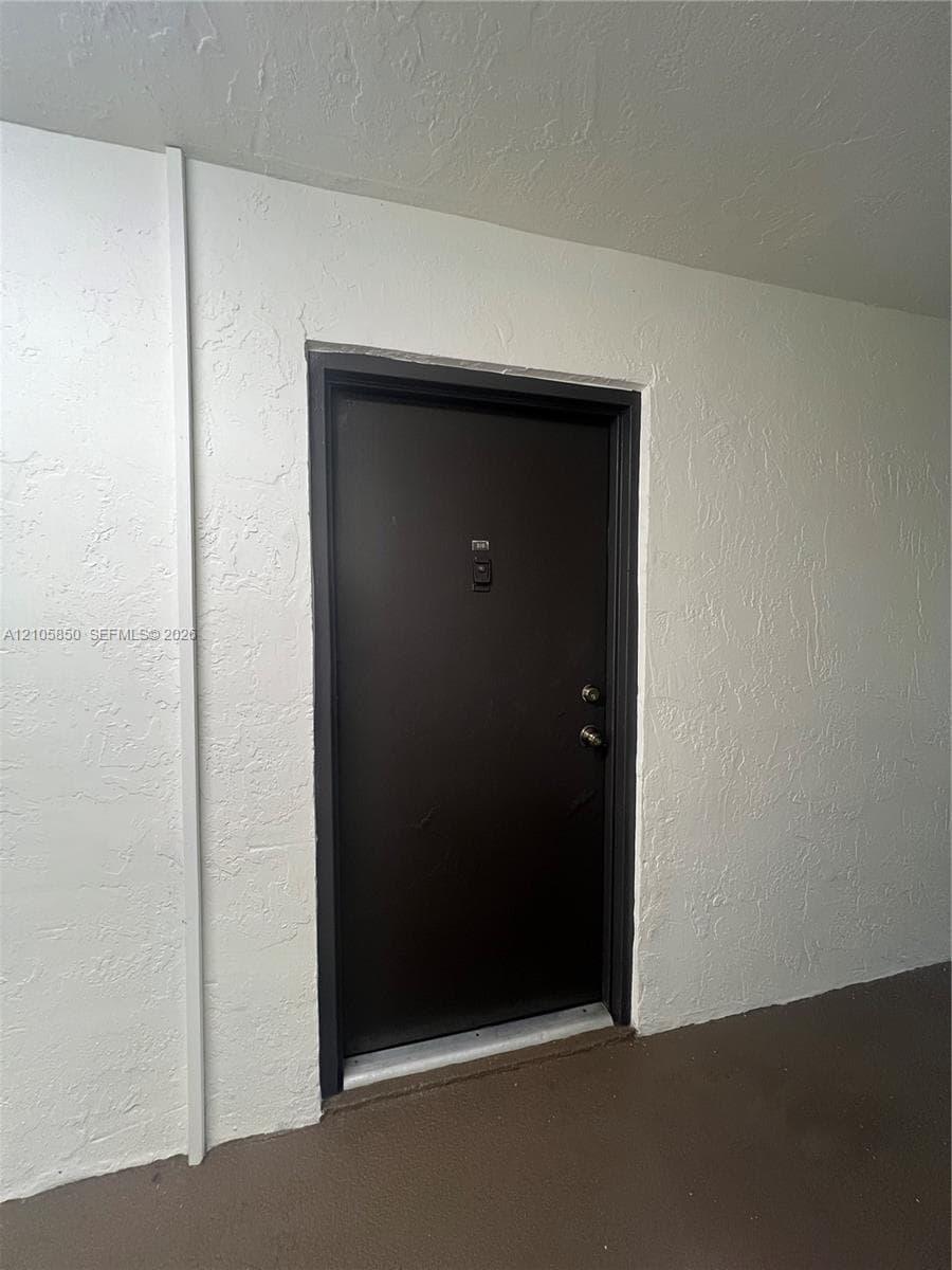 Dark-toned entry door with dual metallic hardware, installed within a textured white wall surround