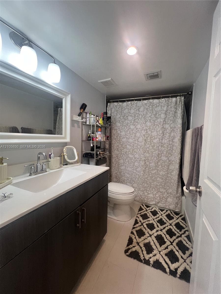 Bathroom featuring a dark wood-finish vanity with a rectangular sink, white stone-surface countertop, chrome hardware, and a framed mirror with three-light fixture