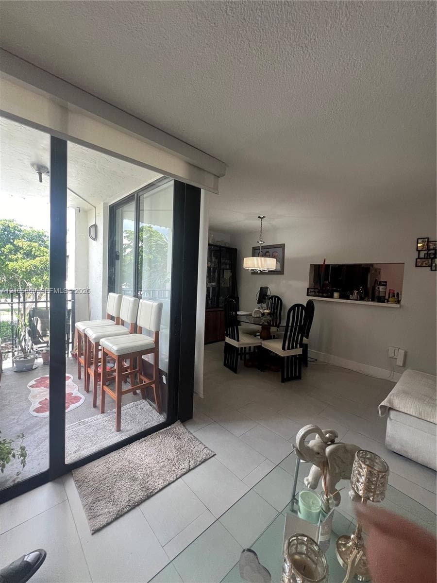 Interior space featuring large format light-toned tile flooring, oversized glass sliding doors, a built-in pass-through wall opening, and a hanging drum-style light fixture