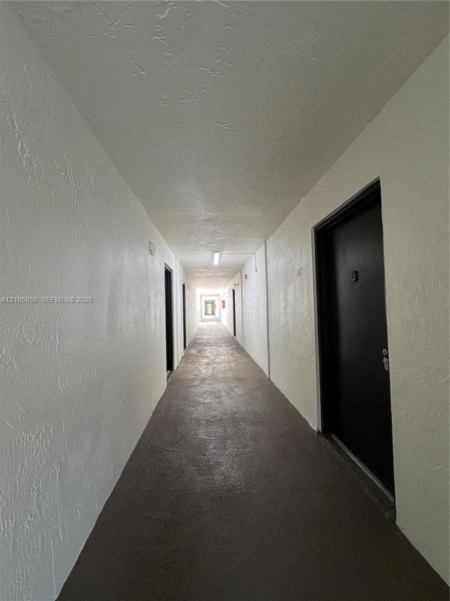 Interior hallway featuring high-contrast black doors, textured white walls, and flush-mount ceiling lighting