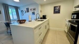Kitchen featuring a white stone-surface island, undermount stainless steel sink with a gooseneck faucet, white shaker-style cabinetry, and light-toned tile flooring