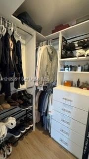 Custom walk-in closet featuring white built-in cabinetry, integrated drawer storage, multi-level clothing rods, tiered shelving, and wood-finish flooring