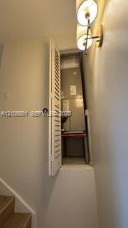 Utility closet featuring a white louvered door, a dual-light wall sconce with a metallic finish, and wood-finish stair treads