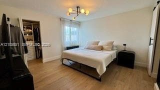 Room featuring light wood-finish flooring, a multi-arm contemporary chandelier, and a walk-in closet with built-in shelving and cabinetry