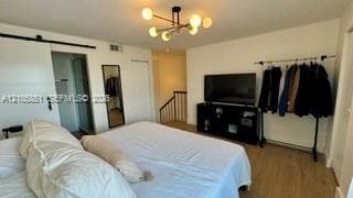 Spacious room featuring wood-finish flooring, a modern sputnik-style chandelier, a white sliding barn door, and a built-in wall-mounted mirror