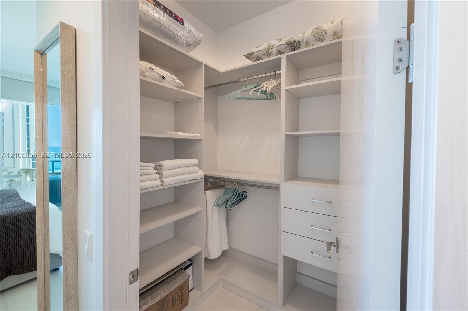 Walk-in closet featuring white custom built-in shelving, multi-level hanging rods, and integrated soft-close drawers with metallic hardware
