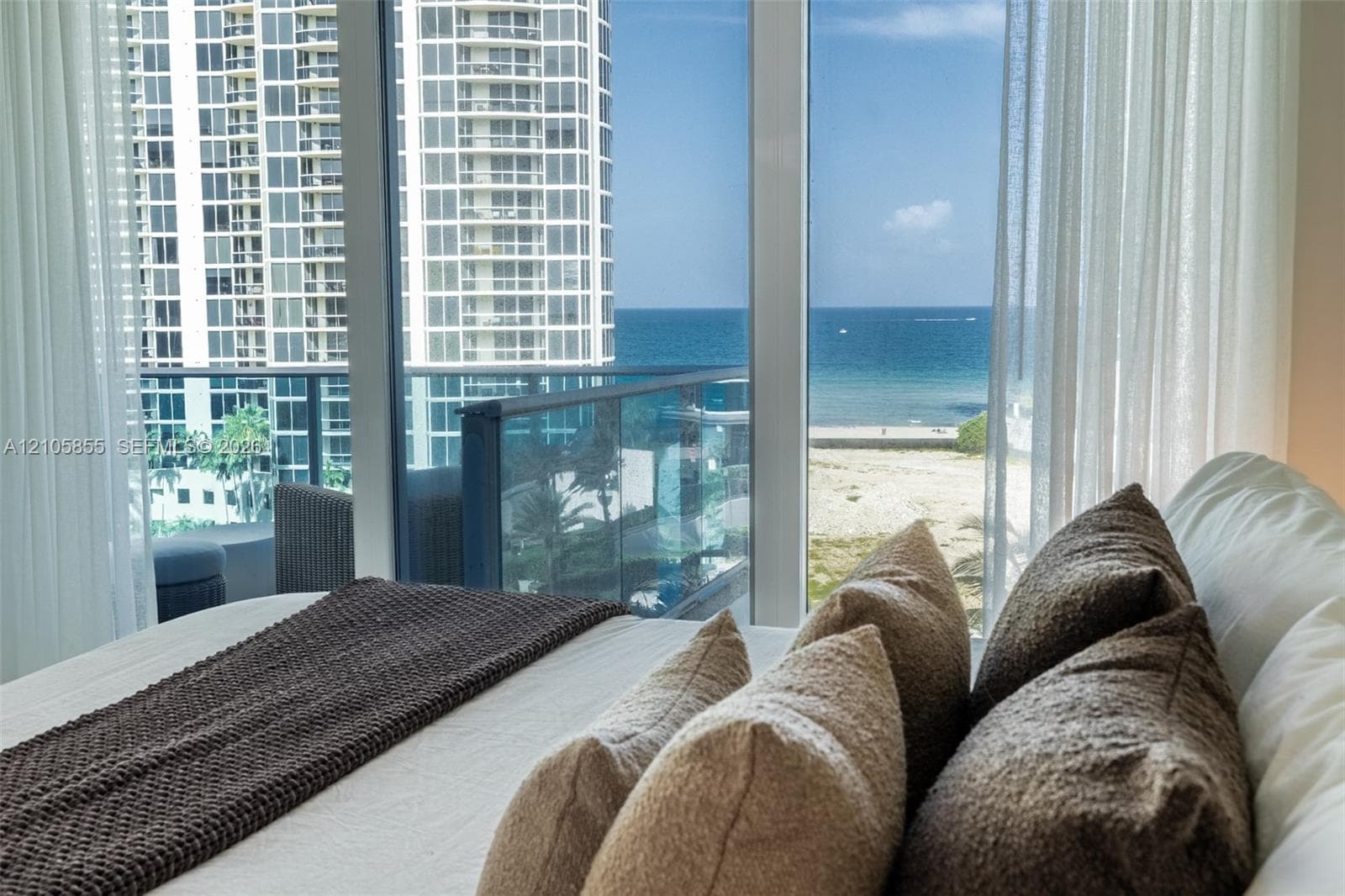 Floor-to-ceiling glass windows, balcony with blue-tinted glass railing, and ocean and coastal exposure