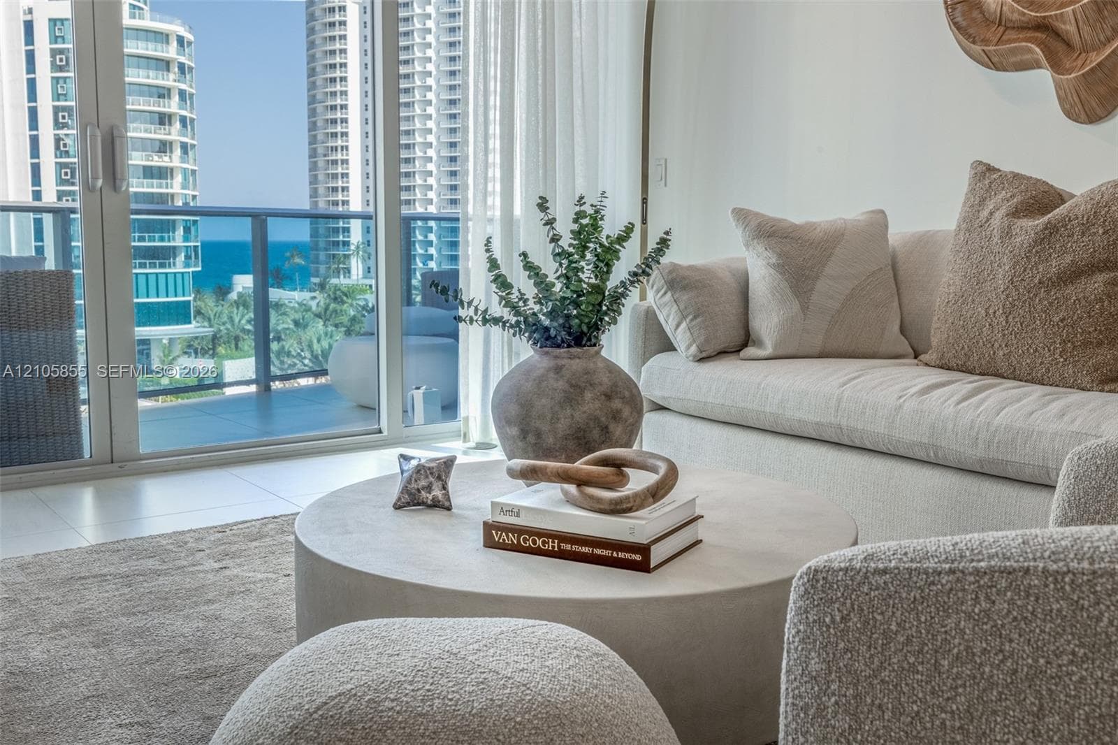 Floor-to-ceiling glass sliding doors, large-format tile flooring, and a private balcony featuring a glass-panel railing overlooking the coastline