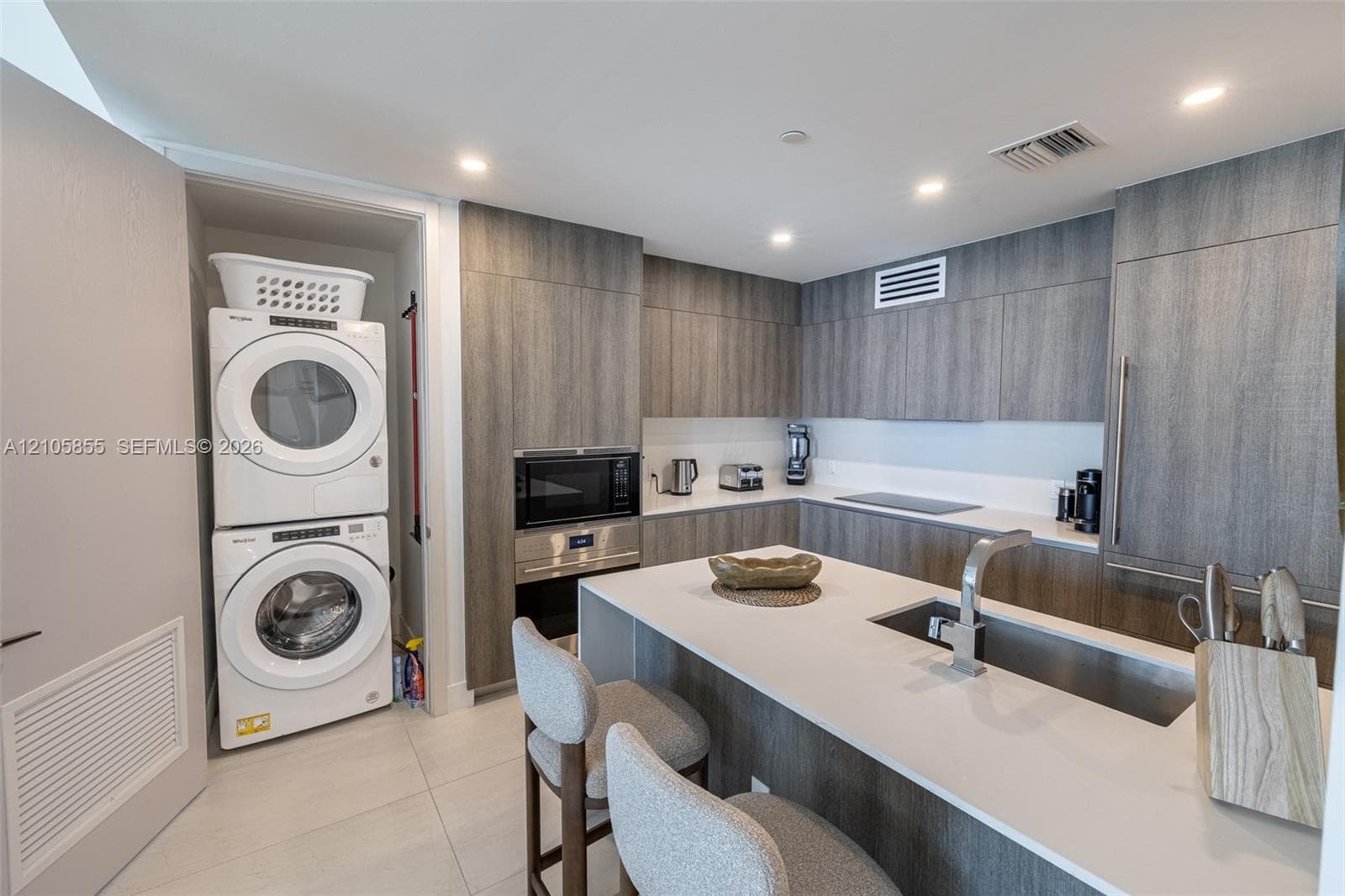 Kitchen featuring flat-panel wood-finish cabinetry, quartz countertops, an integrated island, built-in stainless steel appliances, and a stacked laundry unit