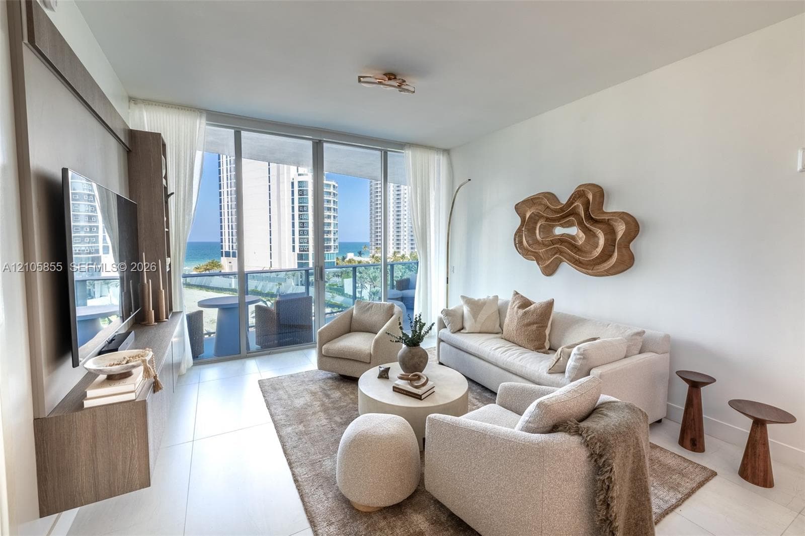 Floor-to-ceiling windows, integrated wood-finish wall paneling, large-format tile flooring, and a private balcony with water exposure