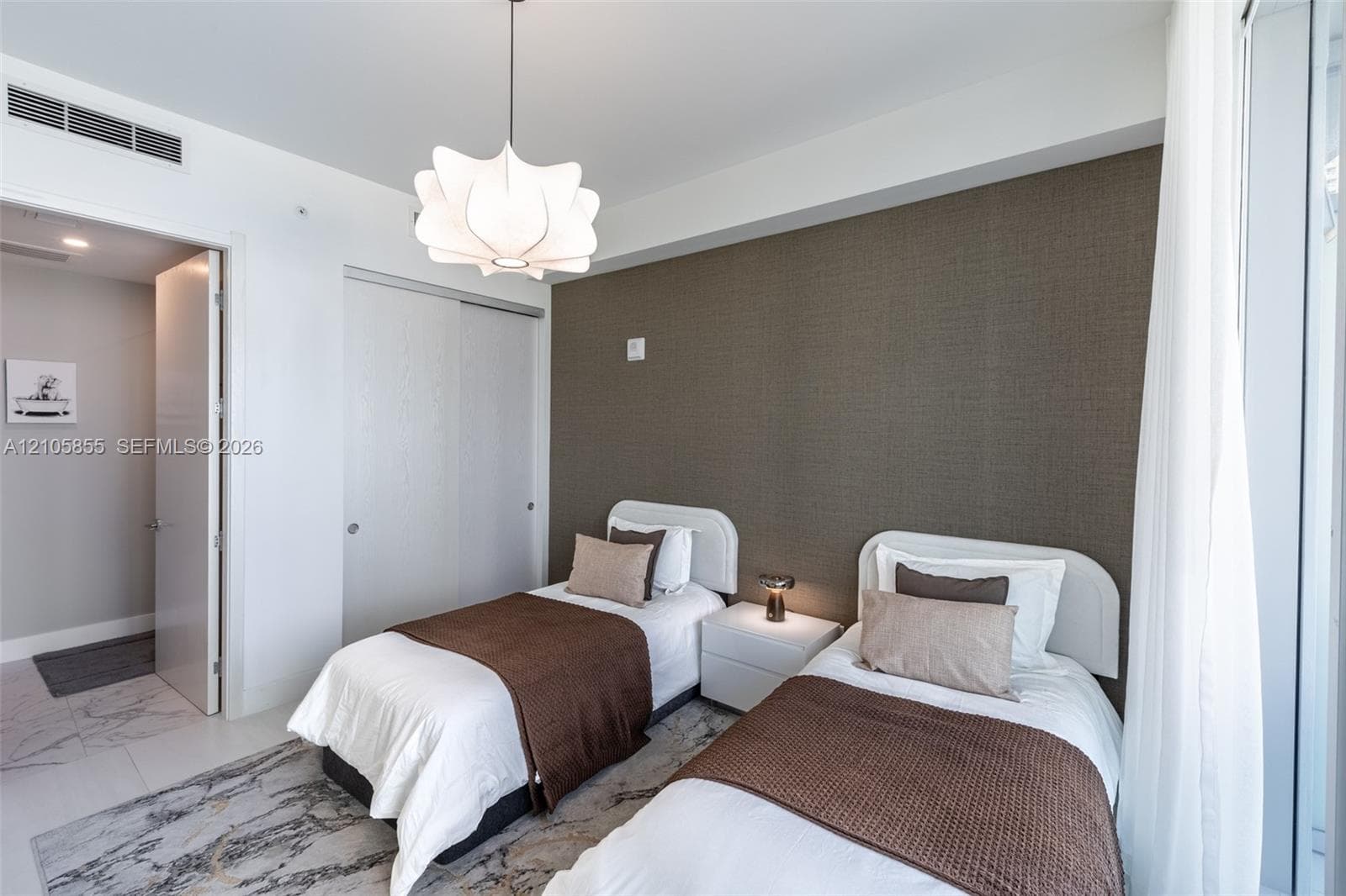 Textured accent wall, sliding door closet with neutral finish, sculptural pendant lighting, and stone-finish tile flooring