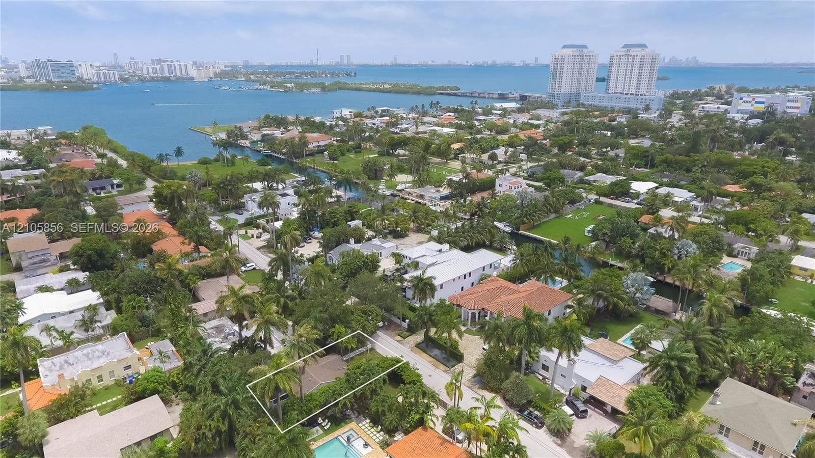 Aerial perspective of a residential property featuring mature palm trees and established landscaping, situated in proximity to coastal waterways and high-rise developments