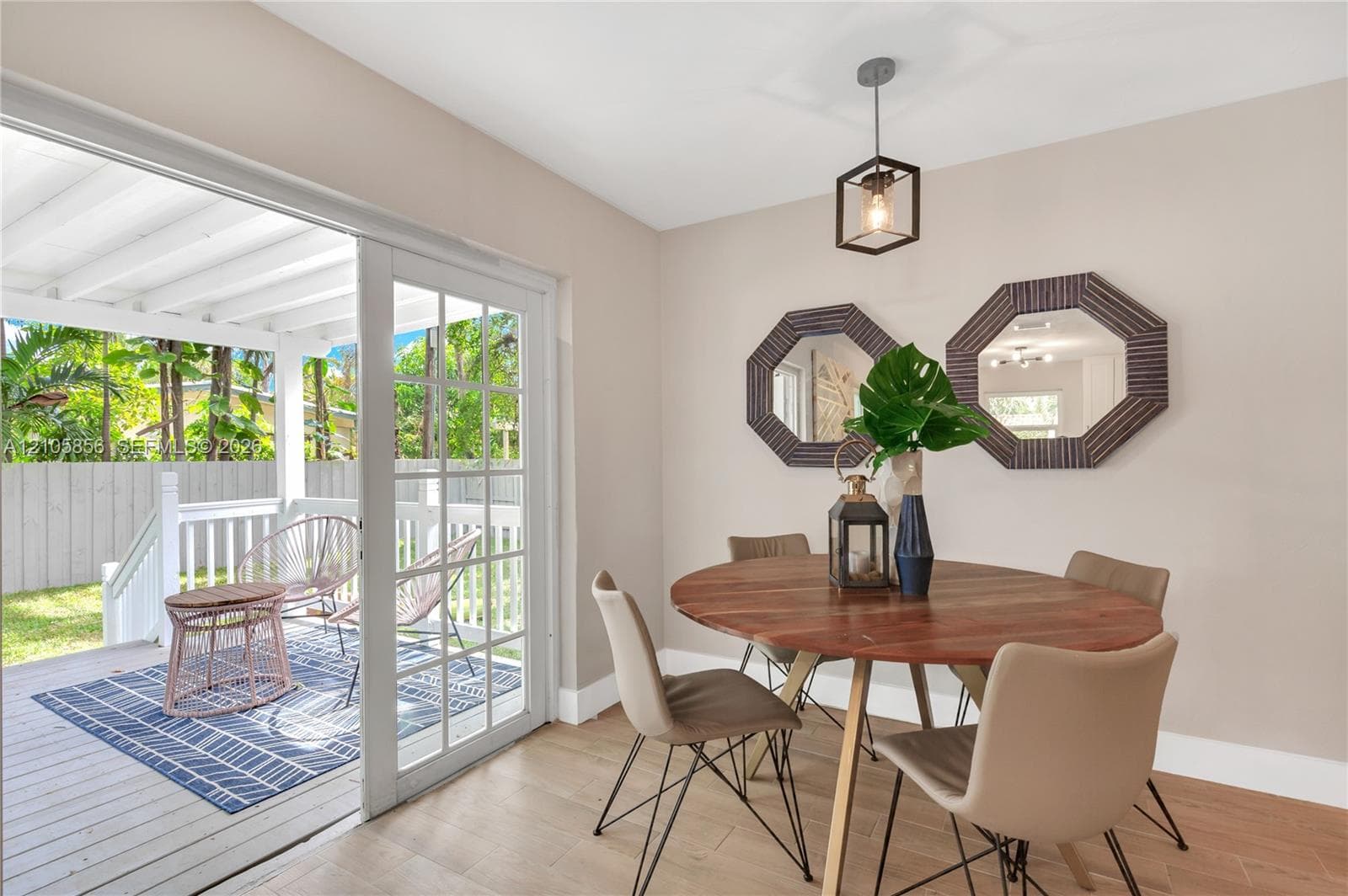 Interior space featuring light wood-finish flooring, a geometric pendant light fixture, and large glass-paned sliding doors opening to a covered wooden deck