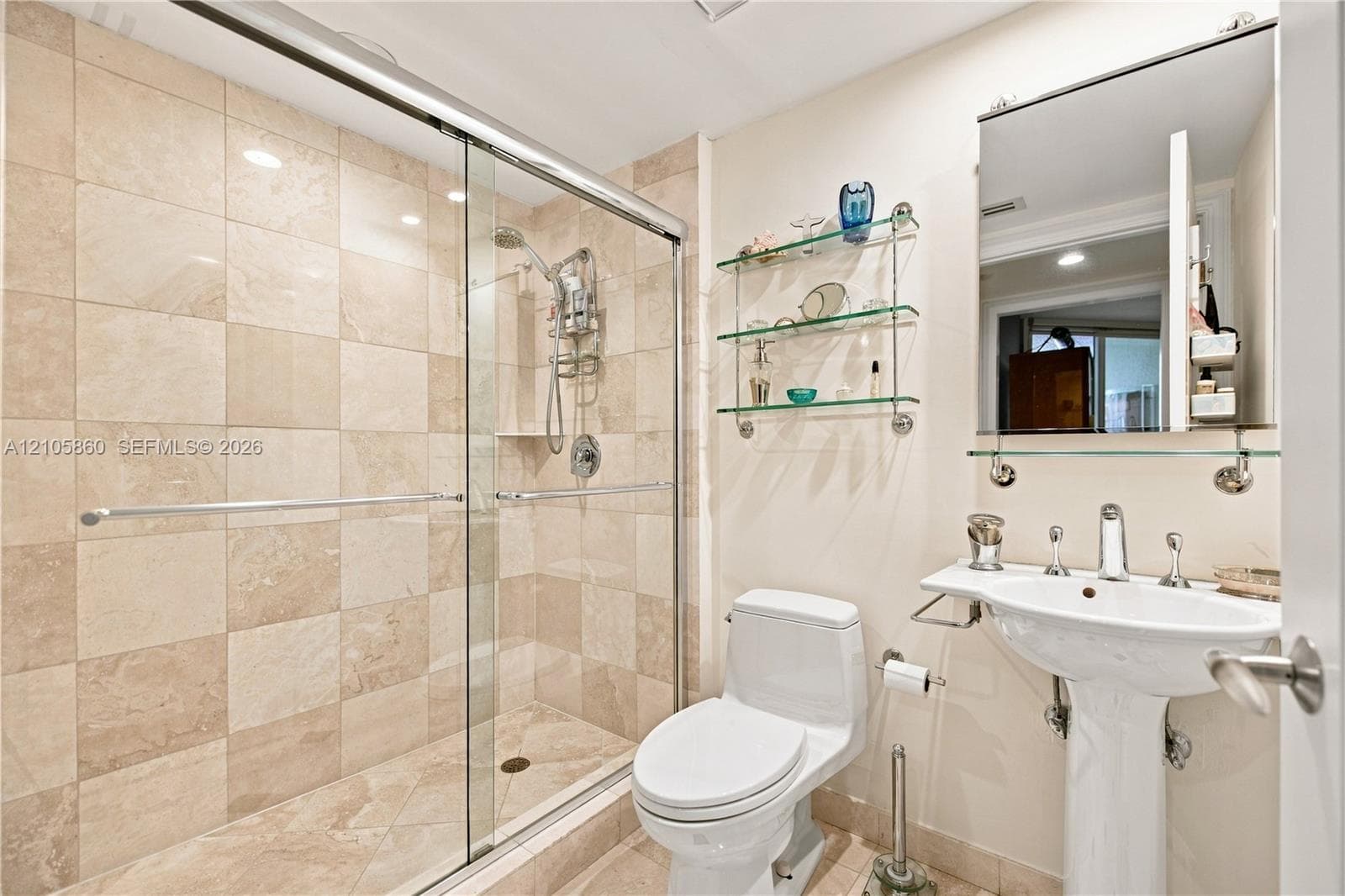 Bathroom featuring a glass-enclosed walk-in shower with stone-finish tile surround, pedestal sink with polished metal fixtures, and built-in glass shelving