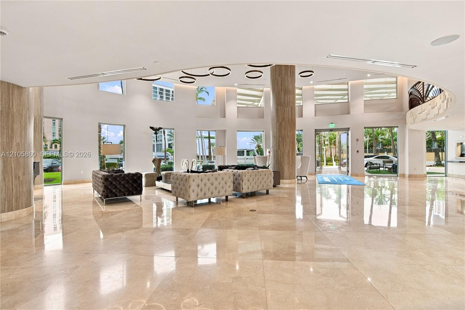 Expansive lobby featuring polished stone flooring, floor-to-ceiling windows, circular recessed ceiling lighting, and stone-clad support columns