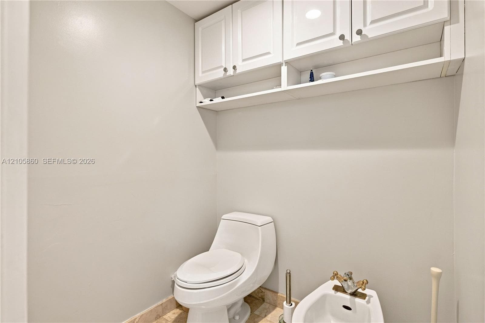 One-piece toilet and bidet fixture, white shaker-style wall-mounted cabinetry with integrated shelving, and natural stone flooring