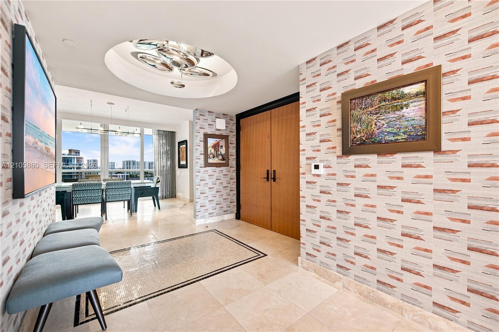 Foyer featuring patterned wallpaper, stone tile flooring with a decorative mosaic inlay, recessed circular ceiling detail with multi-bulb lighting, and wood-finish double doors
