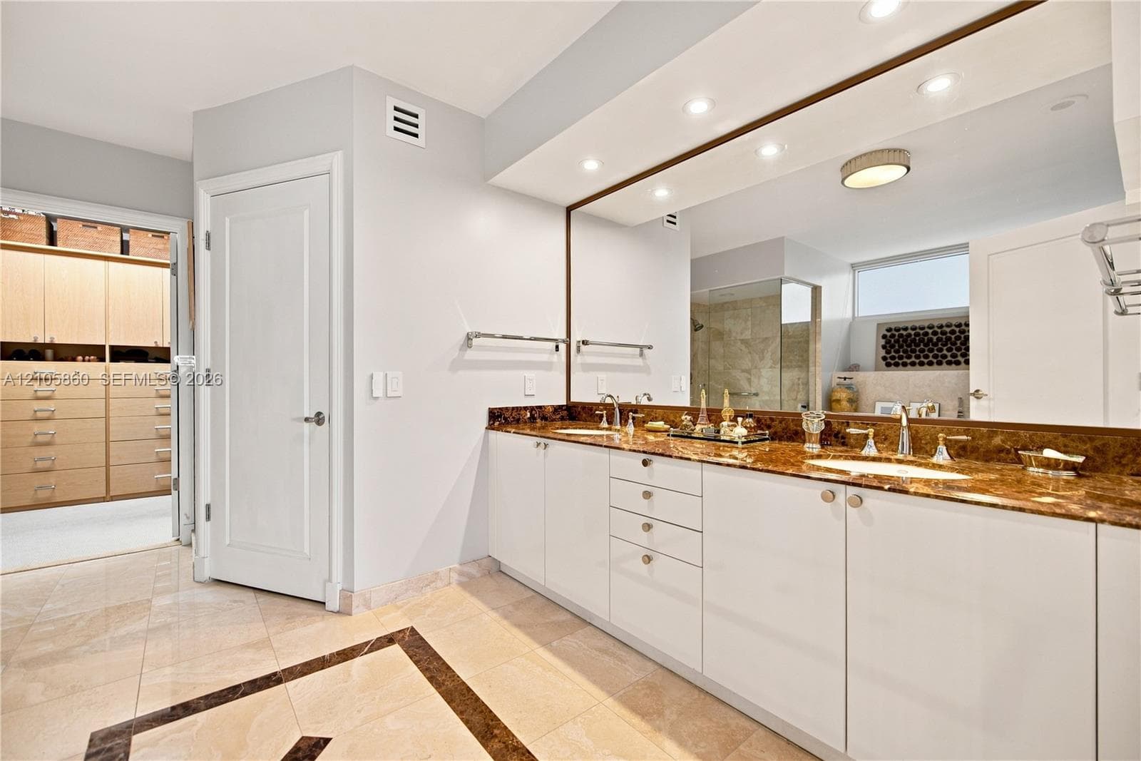 Dual-sink vanity with stone countertop, polished metal fixtures, recessed ceiling lighting, full-width vanity mirror, and built-in closet cabinetry