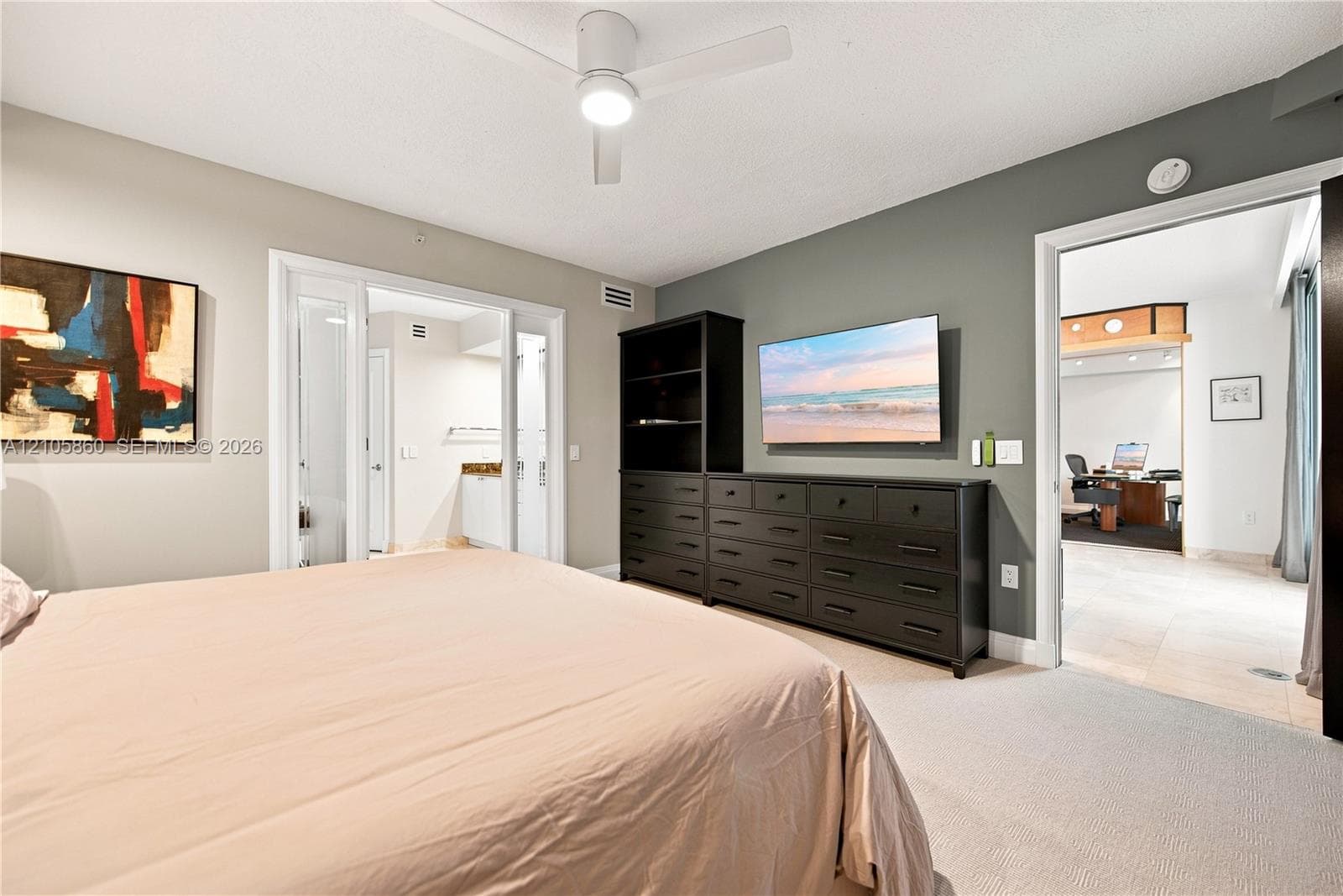 Neutral-toned room featuring a white ceiling fan with integrated lighting, wall-to-wall carpeting, and a dark-finished built-in cabinetry unit