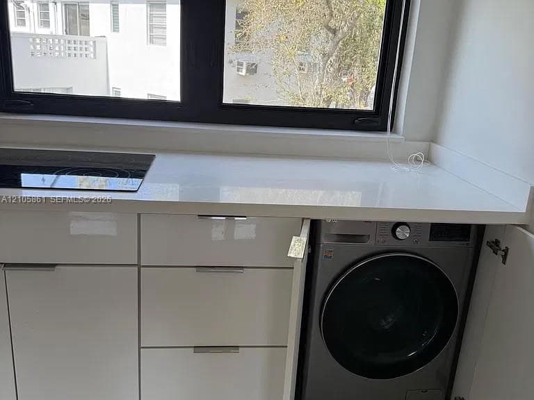 White high-gloss cabinetry featuring sleek metal hardware, a smooth light-toned countertop, a built-in black induction cooktop, and an integrated under-counter appliance