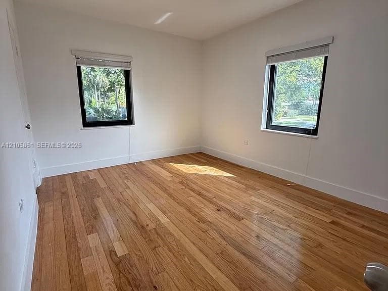Room featuring wood-finish flooring, white walls, and two windows with black frames
