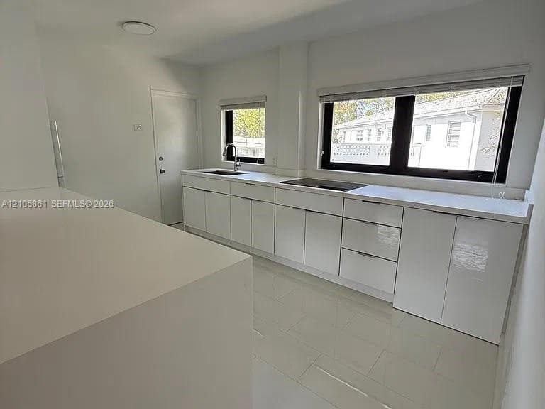 Kitchen featuring gloss-finish cabinetry, solid-surface countertops, tile flooring, and black-framed windows