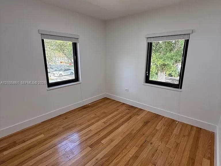 Room featuring wood-finish flooring, white walls, and two windows with black frames