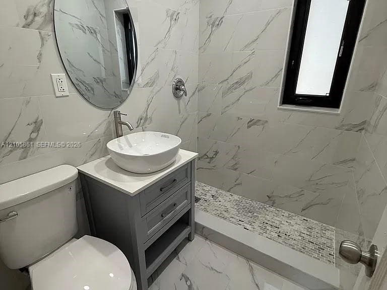 Bathroom featuring large-format veined tile walls, vanity with a white vessel sink, brushed metal fixtures, and a walk-in shower with mosaic tile flooring