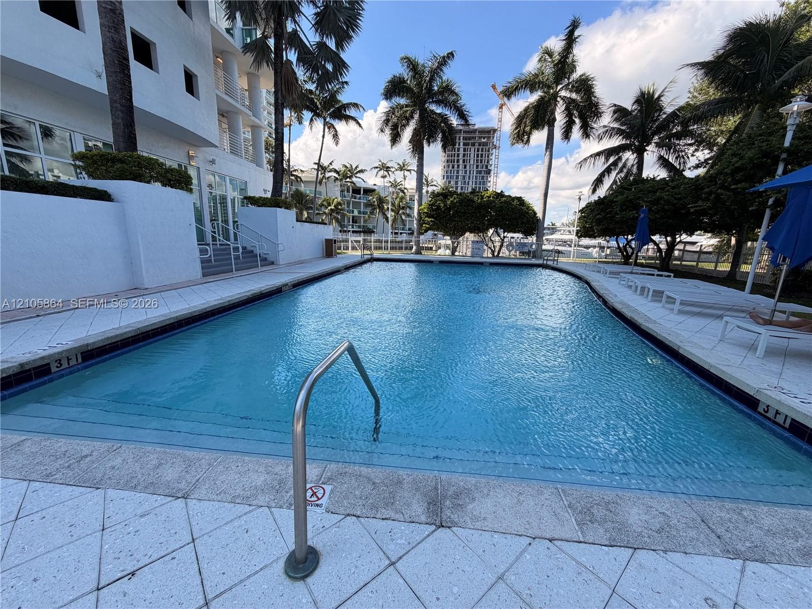 Rectangular swimming pool featuring a tiled deck, stone coping, integrated steps, and a metal handrail