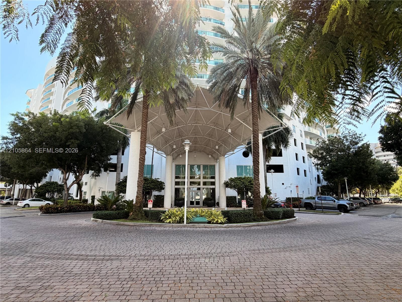 High-rise building exterior featuring a covered porte-cochère entrance, glass-paneled double doors, paved circular drive, and landscaped grounds