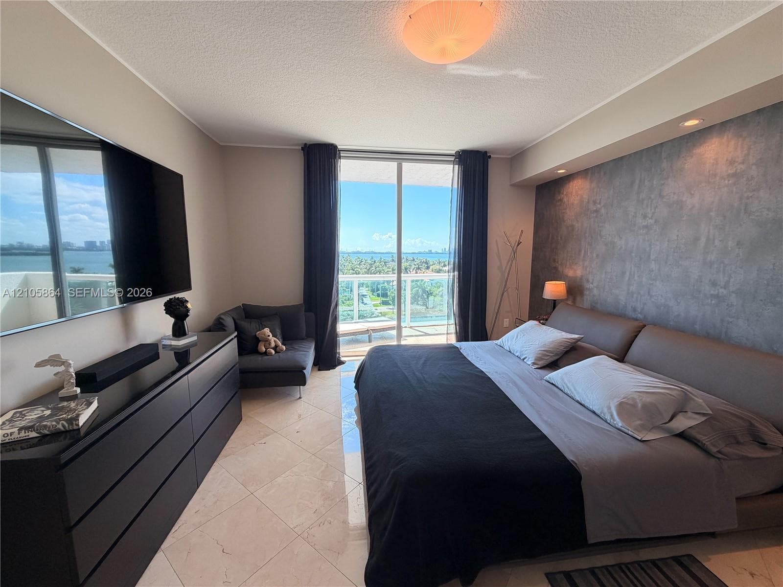 Floor-to-ceiling sliding glass doors opening to a balcony, large-format tile flooring, textured accent wall, and recessed ceiling lighting