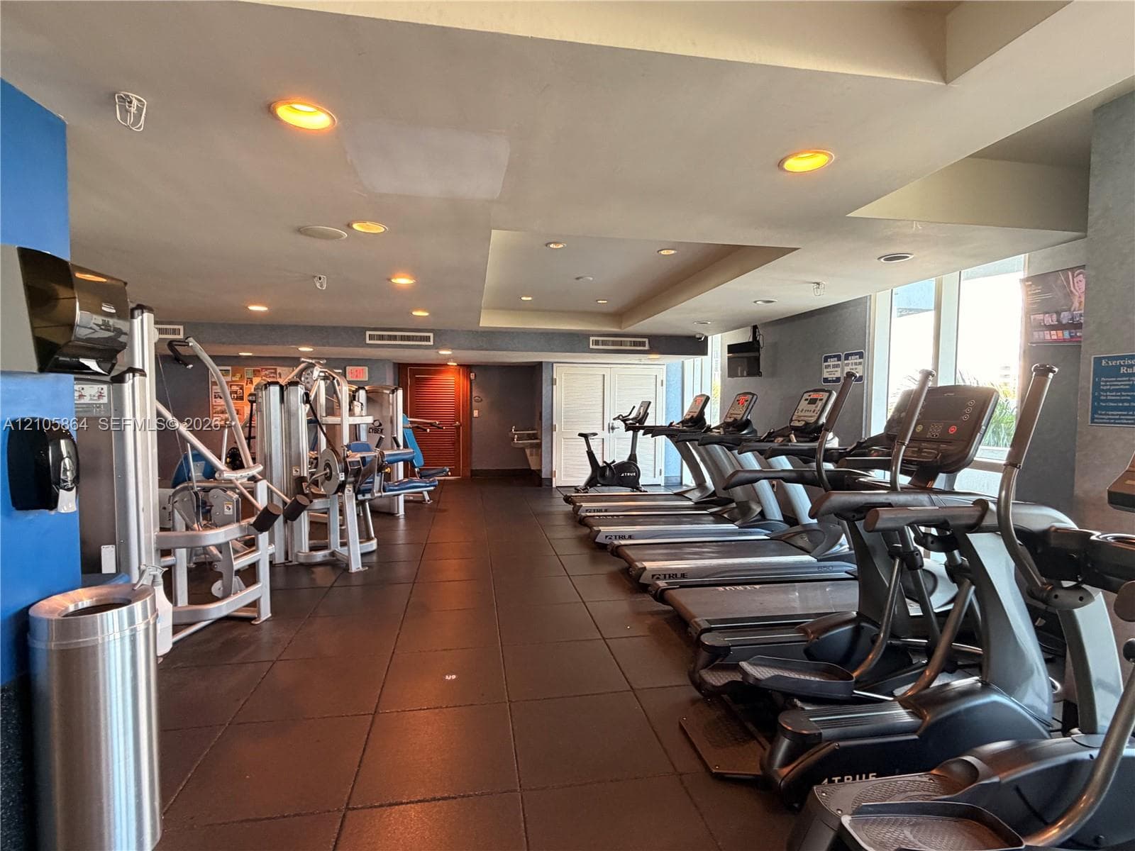 Fitness center featuring rubberized tile flooring, recessed lighting, floor-to-ceiling windows, and multiple built-in weight and cardiovascular training stations