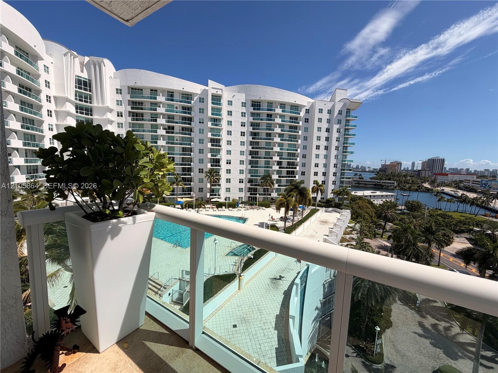 Private balcony with glass and metal railing, overlooking a swimming pool, sun deck, and coastal waterway