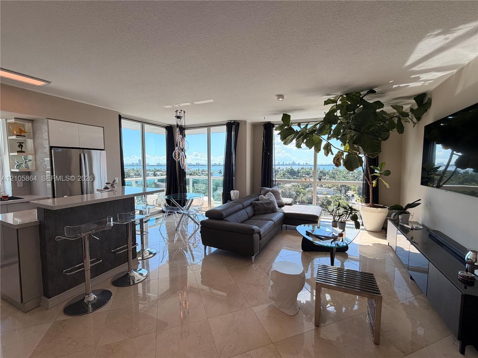Open-concept living space featuring floor-to-ceiling windows, polished stone flooring, stainless steel kitchen appliances, and a breakfast bar with stone-finish surfacing